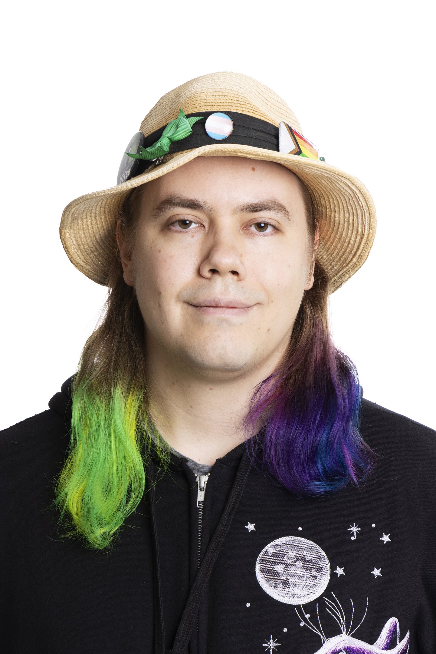 My official candidate picture. On my hat you see a green bow, a trans flag pin and a pride flag pin; my hair is dyed green and a bit of yellow on one side and purple, blue and pink on the other.