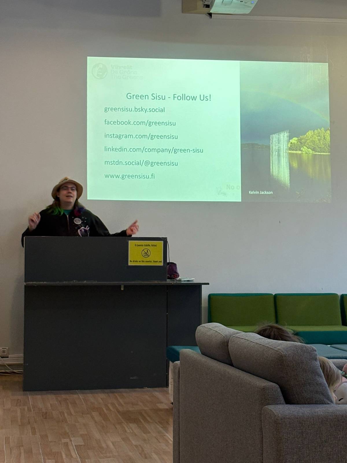 Me, speaking at a podium in front of a slide showing Green Sisu's social media handles.